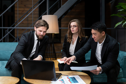Two businessmen and a businesswoman looking at a computer and discussing burn out, brown out, and burn out