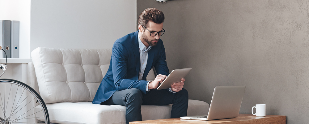 Picture of businessman sitting on sofa with tablet PC and notebook on table